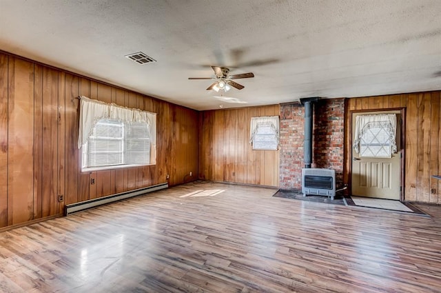 unfurnished living room featuring a healthy amount of sunlight, a textured ceiling, a wood stove, and a baseboard radiator