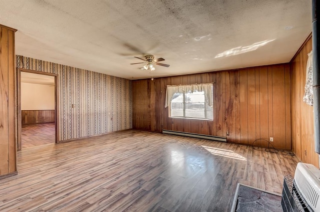 spare room featuring ceiling fan, wood walls, light hardwood / wood-style flooring, a textured ceiling, and a baseboard radiator