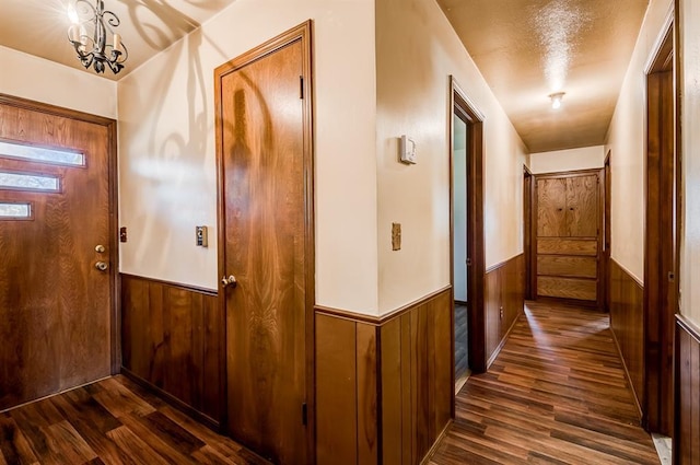 interior space with dark wood-type flooring, a chandelier, and wood walls