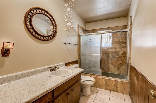 full bathroom featuring toilet, combined bath / shower with glass door, wooden walls, tile patterned flooring, and vanity