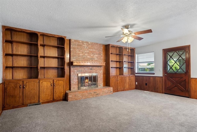 unfurnished living room with a brick fireplace, carpet, wood walls, and a textured ceiling