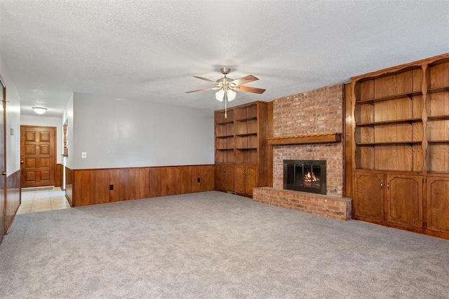 unfurnished living room with ceiling fan, a textured ceiling, light carpet, and a fireplace