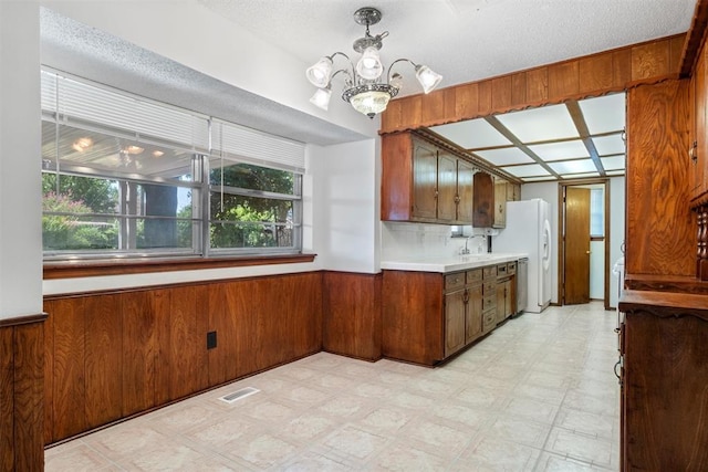 kitchen with hanging light fixtures, white refrigerator, a textured ceiling, and wooden walls