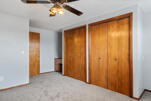 unfurnished bedroom featuring a textured ceiling, multiple closets, light colored carpet, and ceiling fan