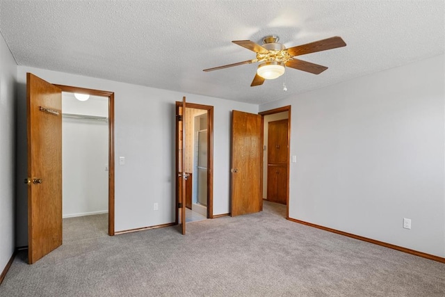 unfurnished bedroom with a spacious closet, a textured ceiling, light carpet, a closet, and ceiling fan