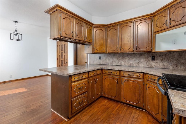 kitchen featuring kitchen peninsula, pendant lighting, dark hardwood / wood-style floors, backsplash, and black / electric stove