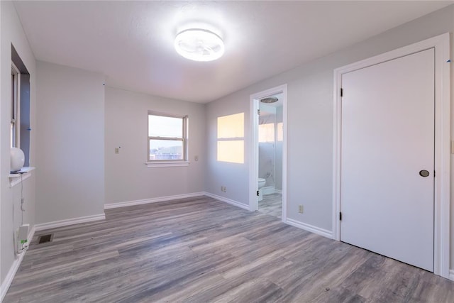 unfurnished bedroom with ensuite bathroom and light wood-type flooring