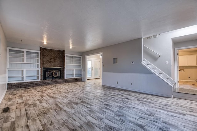 unfurnished living room with built in shelves, a brick fireplace, a textured ceiling, and light hardwood / wood-style floors