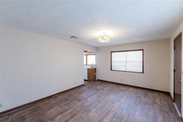 spare room featuring a textured ceiling, dark wood-type flooring, and an inviting chandelier