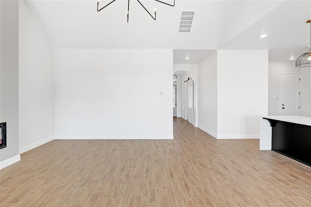 unfurnished living room featuring a notable chandelier and light hardwood / wood-style floors