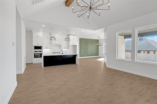kitchen featuring pendant lighting, white cabinetry, an island with sink, built in microwave, and stainless steel oven