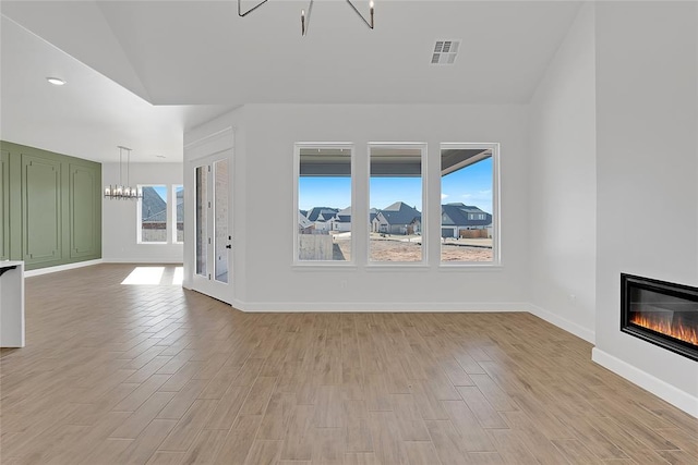 unfurnished living room featuring an inviting chandelier, light hardwood / wood-style flooring, and lofted ceiling