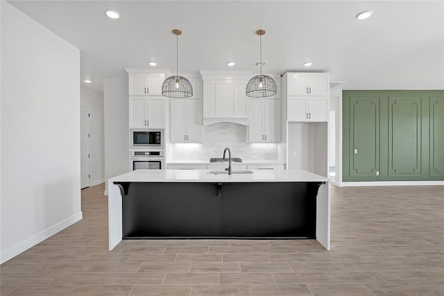 kitchen with pendant lighting, an island with sink, white cabinets, built in microwave, and oven