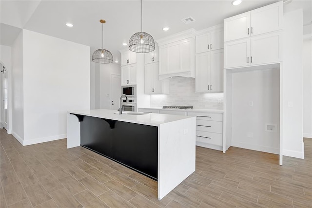 kitchen featuring sink, stainless steel appliances, an island with sink, white cabinets, and decorative light fixtures