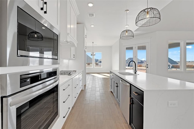 kitchen with pendant lighting, sink, stainless steel appliances, an island with sink, and white cabinets