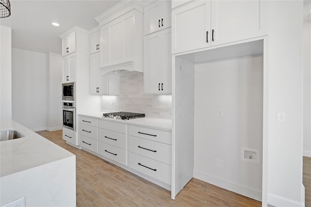 kitchen with white cabinetry, tasteful backsplash, custom range hood, stainless steel appliances, and light hardwood / wood-style floors