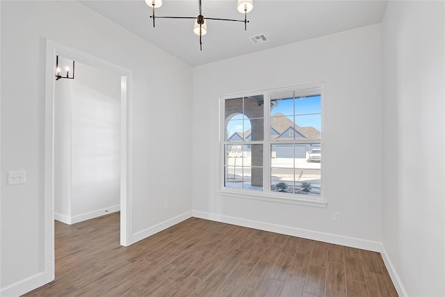spare room featuring wood-type flooring and a notable chandelier
