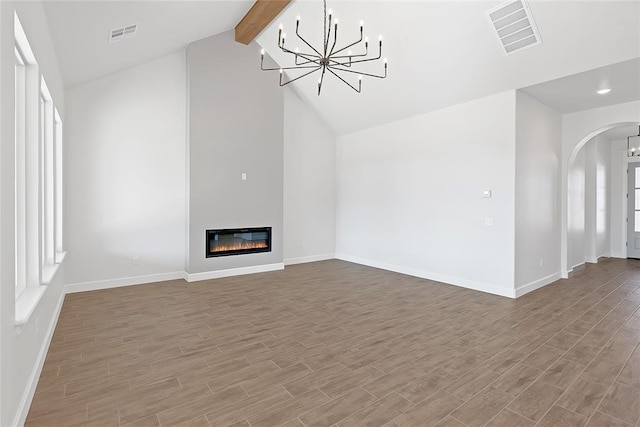 unfurnished living room with an inviting chandelier, beam ceiling, light hardwood / wood-style flooring, and a wealth of natural light