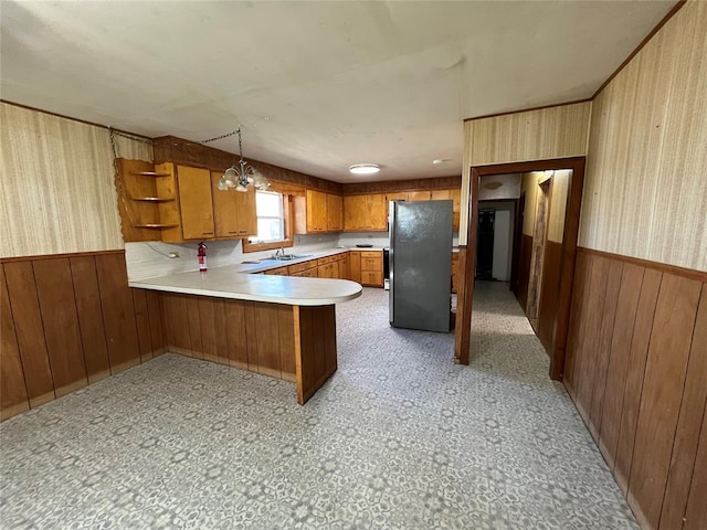 kitchen featuring wood walls, kitchen peninsula, stainless steel fridge, pendant lighting, and an inviting chandelier