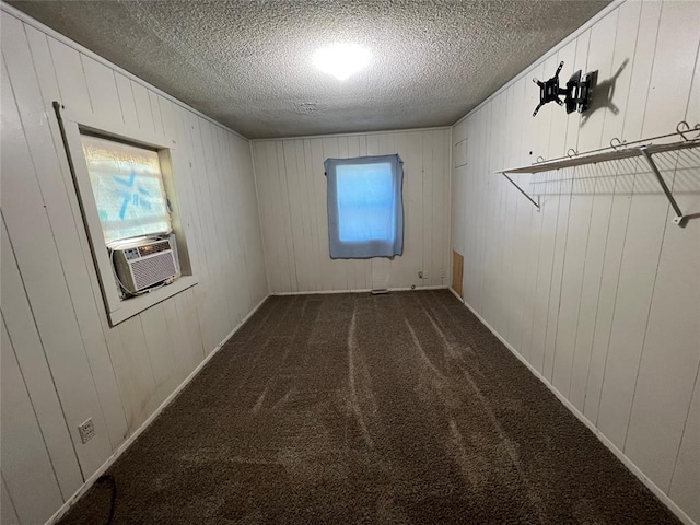 unfurnished room featuring cooling unit, dark carpet, wood walls, and a textured ceiling