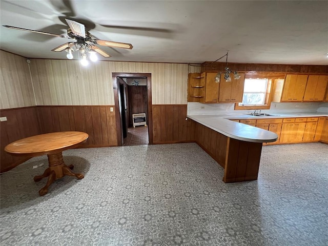 kitchen with wood walls, heating unit, kitchen peninsula, ceiling fan, and sink