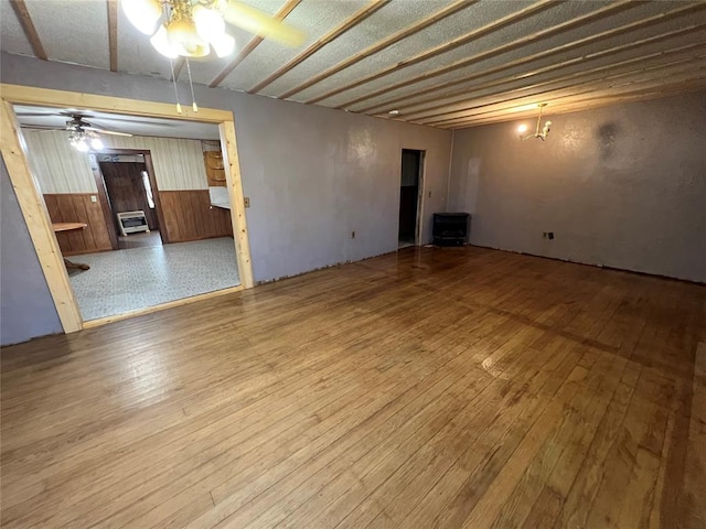 interior space featuring ceiling fan with notable chandelier, hardwood / wood-style flooring, wooden walls, and heating unit