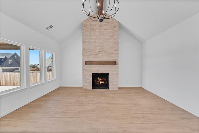 unfurnished living room with an inviting chandelier, a fireplace, light hardwood / wood-style flooring, and vaulted ceiling