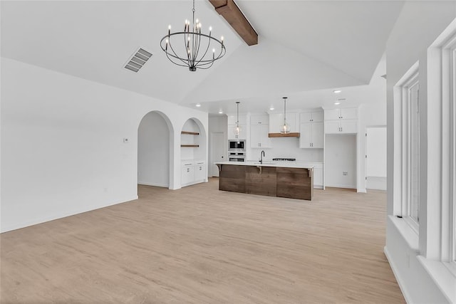 kitchen featuring built in features, white cabinetry, hanging light fixtures, stainless steel appliances, and a center island with sink