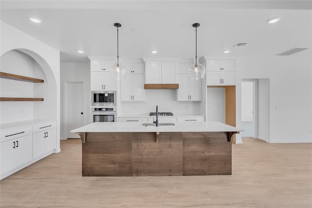 kitchen with pendant lighting, sink, a kitchen island with sink, white cabinetry, and stainless steel appliances