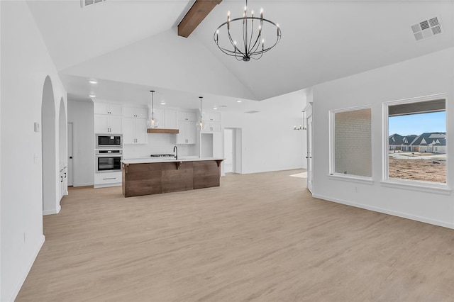 kitchen with decorative light fixtures, built in microwave, stainless steel oven, a center island with sink, and beam ceiling