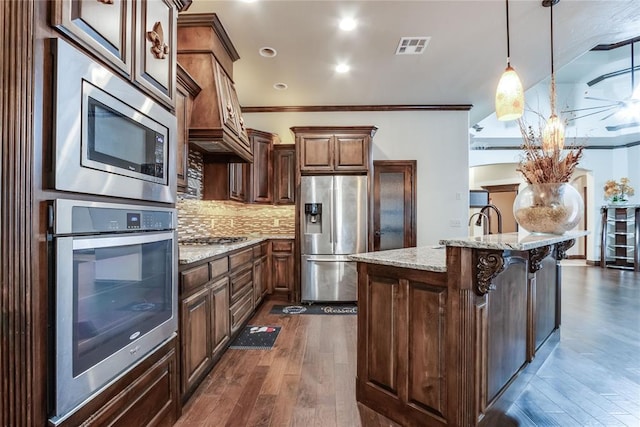 kitchen featuring decorative light fixtures, tasteful backsplash, a center island, light stone countertops, and appliances with stainless steel finishes