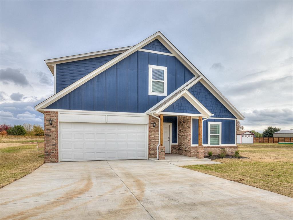 view of front of property with board and batten siding, a front lawn, concrete driveway, and brick siding