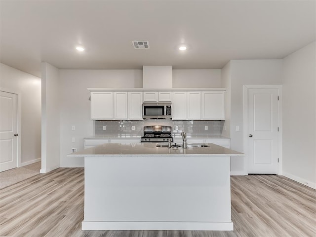 kitchen with light wood-style flooring, stove, a sink, visible vents, and stainless steel microwave