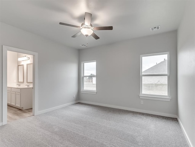 unfurnished bedroom featuring light carpet, baseboards, visible vents, a ceiling fan, and ensuite bathroom