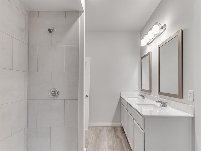 bathroom featuring baseboards, wood finished floors, a sink, and tiled shower