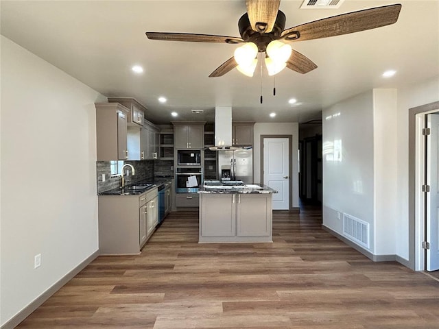 kitchen with appliances with stainless steel finishes, a kitchen island, sink, backsplash, and gray cabinets