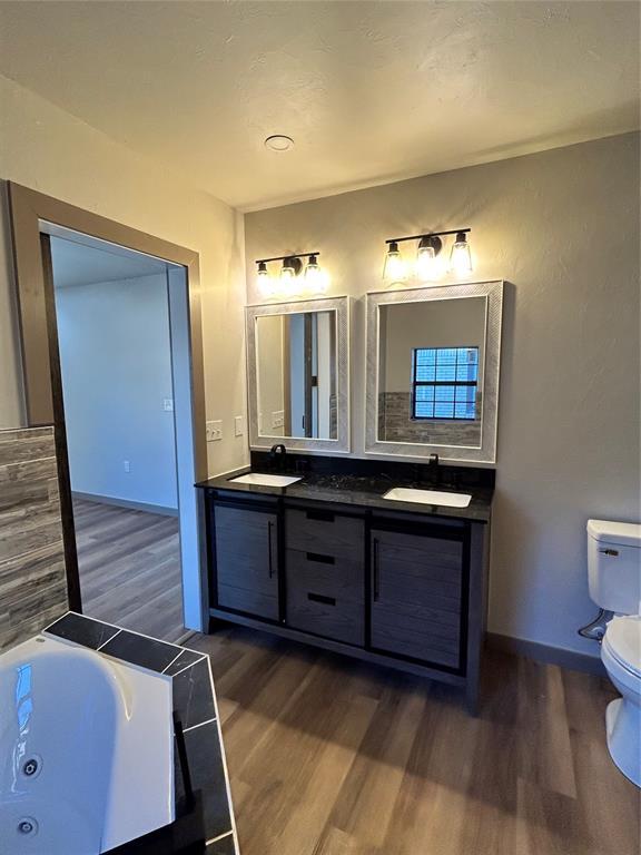 bathroom with toilet, wood-type flooring, vanity, and a washtub