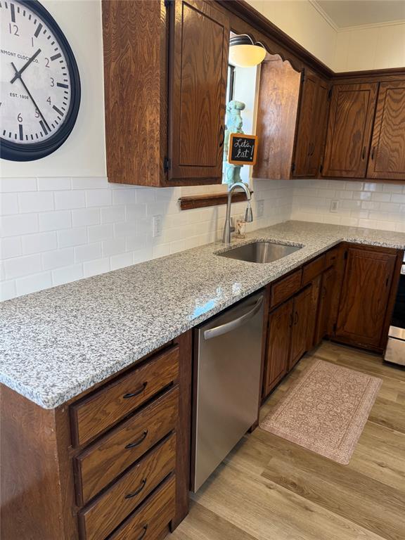 kitchen featuring a sink, light wood-style floors, stainless steel dishwasher, backsplash, and light stone countertops