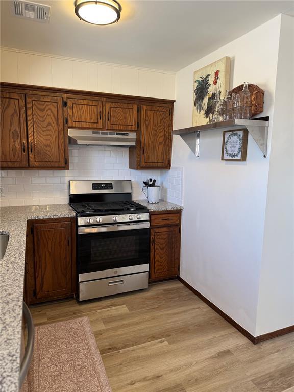 kitchen featuring light wood-style flooring, under cabinet range hood, visible vents, backsplash, and stainless steel range with gas stovetop