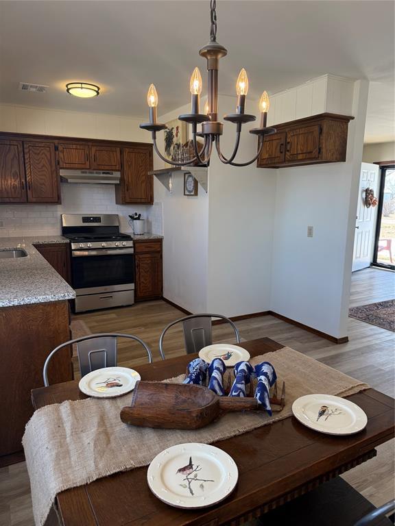 kitchen featuring under cabinet range hood, visible vents, tasteful backsplash, gas range, and an inviting chandelier