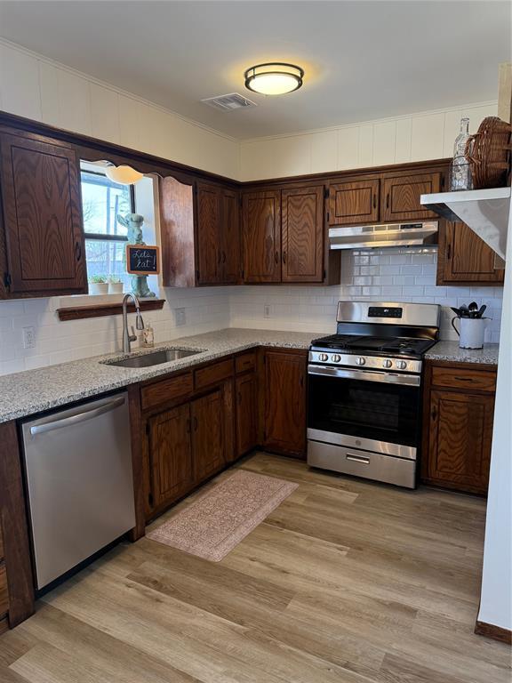 kitchen with appliances with stainless steel finishes, a sink, light wood-style flooring, and under cabinet range hood