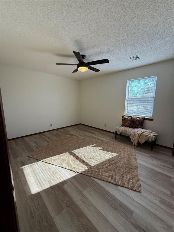 unfurnished bedroom featuring ceiling fan, a textured ceiling, wood finished floors, and visible vents