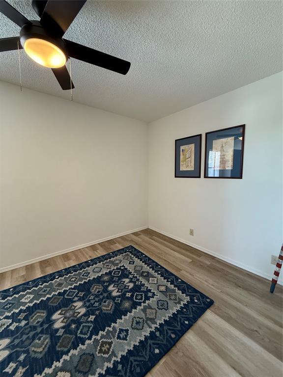 unfurnished room featuring ceiling fan, a textured ceiling, baseboards, and wood finished floors