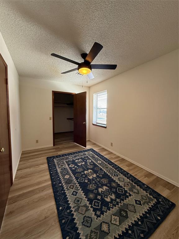 interior space with baseboards, a textured ceiling, a ceiling fan, and light wood-style floors