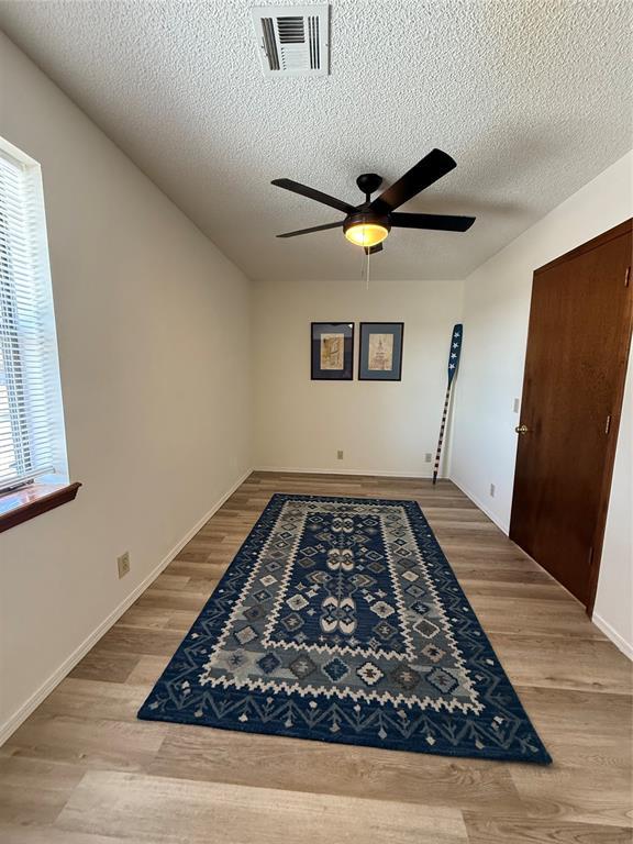 spare room with baseboards, visible vents, a ceiling fan, a textured ceiling, and light wood-style floors