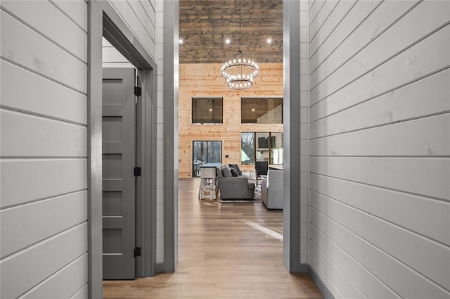 corridor featuring light wood-type flooring, an inviting chandelier, and wooden walls