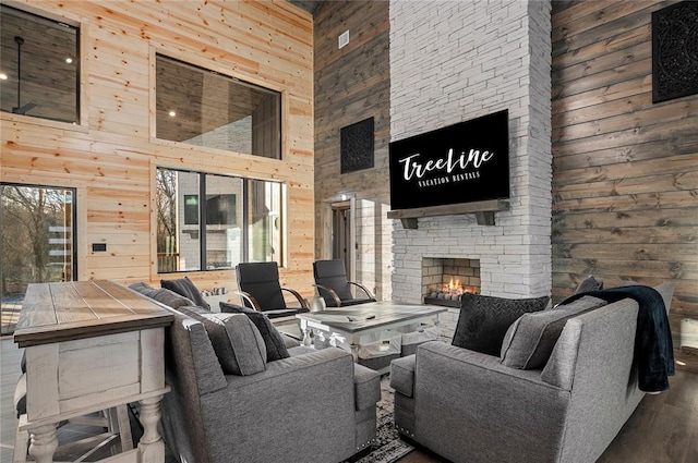 living room with hardwood / wood-style floors, an outdoor stone fireplace, wood walls, and a towering ceiling