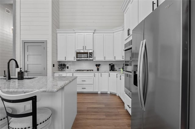 kitchen with light stone counters, a breakfast bar, white cabinets, and stainless steel appliances