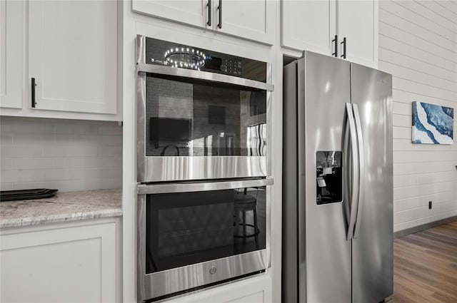 kitchen featuring white cabinets, light stone counters, stainless steel appliances, and hardwood / wood-style flooring