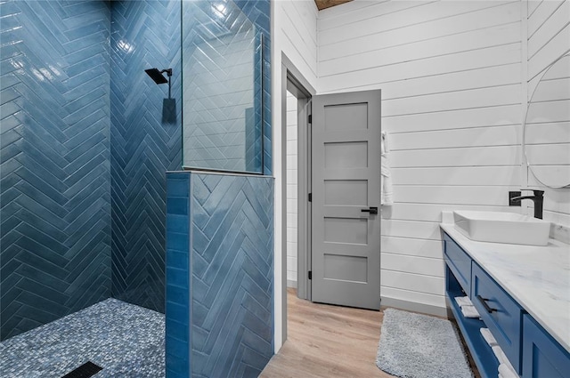 bathroom with vanity, wood-type flooring, wooden walls, and tiled shower